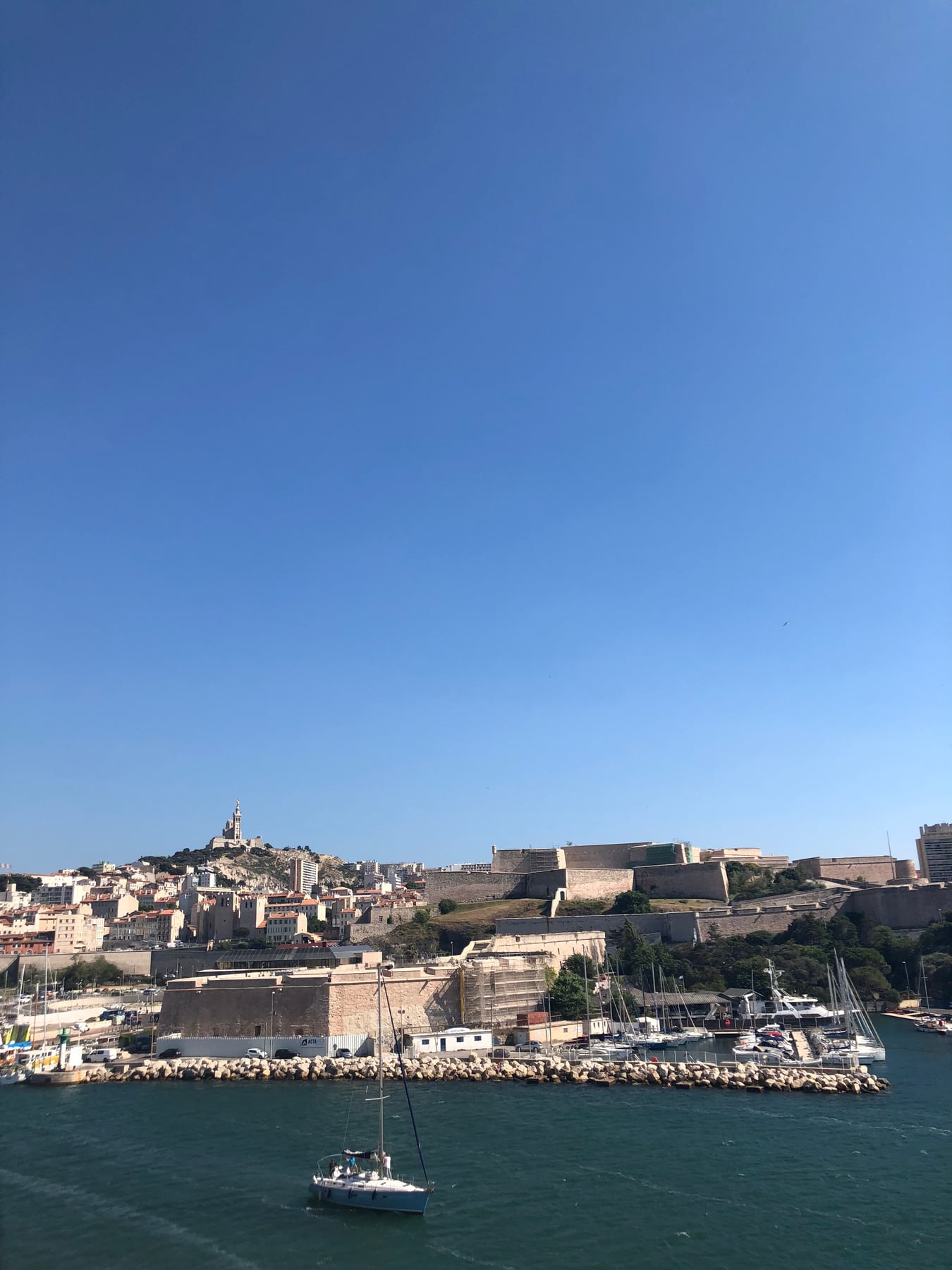 Sailboat crossing Marseille harbor beneath the city skyline