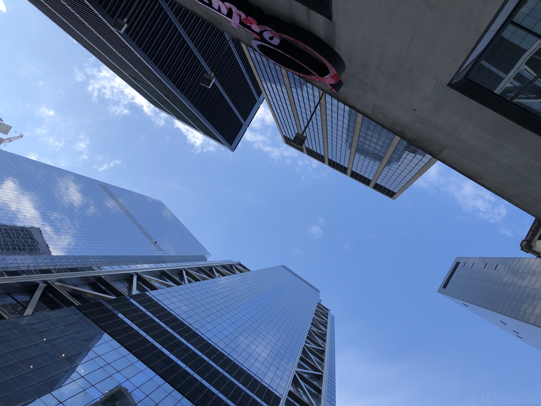 Looking up between reflective Manhattan skyscrapers into a blue sky