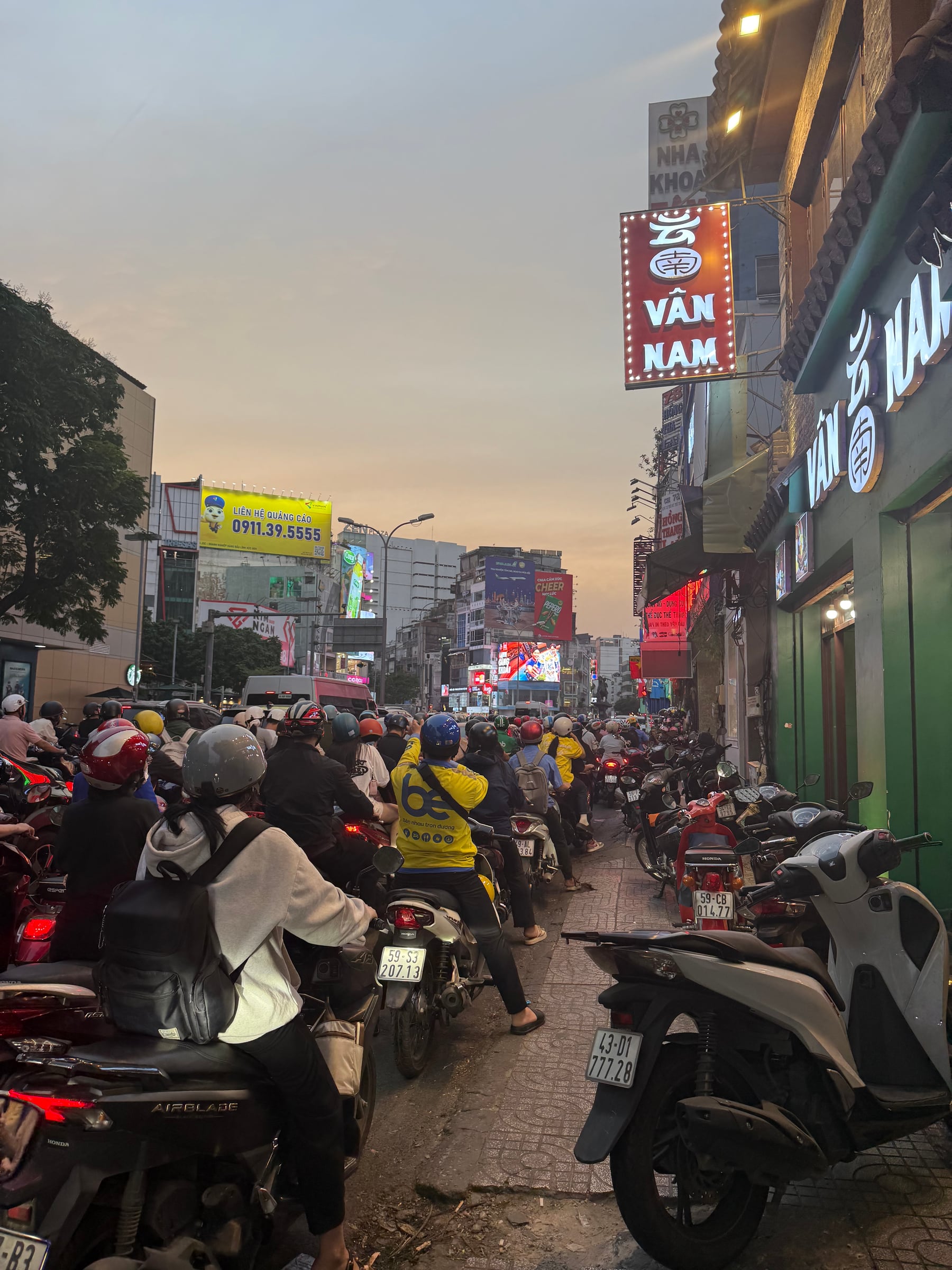 Dense evening motorbike traffic beneath illuminated signs